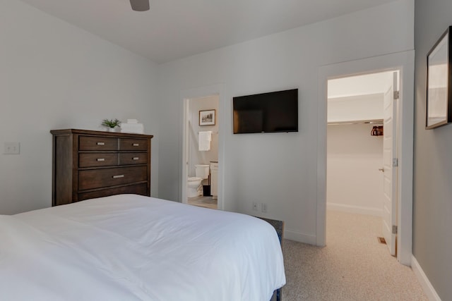 carpeted bedroom with a spacious closet, baseboards, ensuite bath, and a ceiling fan