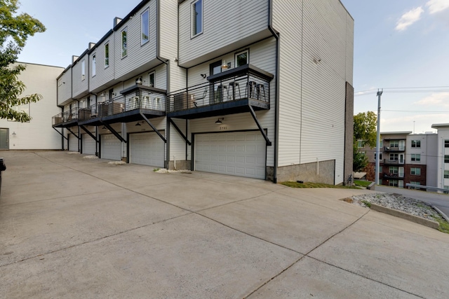 rear view of property with an attached garage, a balcony, and concrete driveway