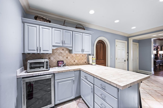 kitchen with beverage cooler, ornamental molding, a peninsula, a sink, and tasteful backsplash