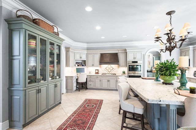 kitchen with custom exhaust hood, a chandelier, backsplash, appliances with stainless steel finishes, and light stone counters