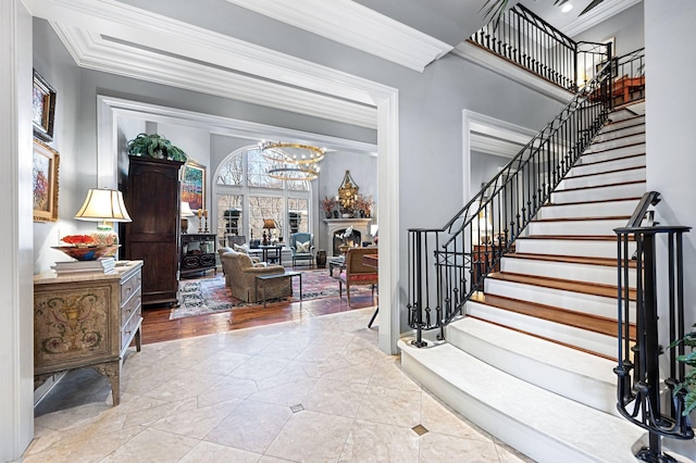 entryway with stairway, crown molding, a chandelier, and a fireplace