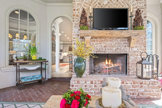 living room with brick floors, ornamental molding, a fireplace, and arched walkways