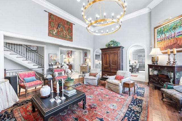 living room featuring arched walkways, wood-type flooring, a chandelier, ornamental molding, and a high ceiling