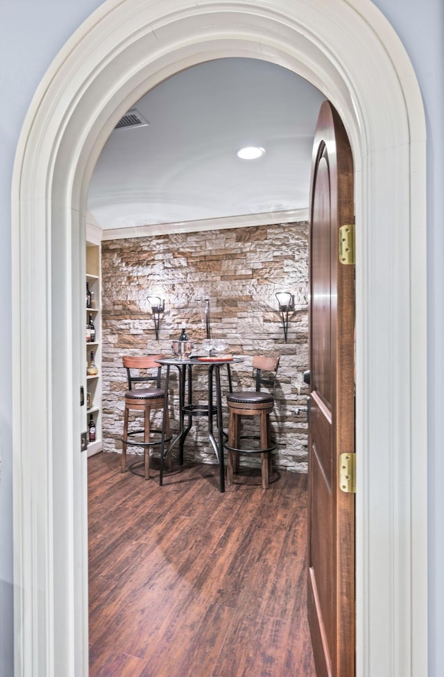 wine area with arched walkways, wood finished floors, and built in shelves
