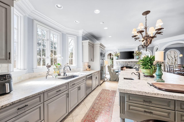 kitchen featuring stainless steel appliances, gray cabinets, a sink, a chandelier, and a lit fireplace