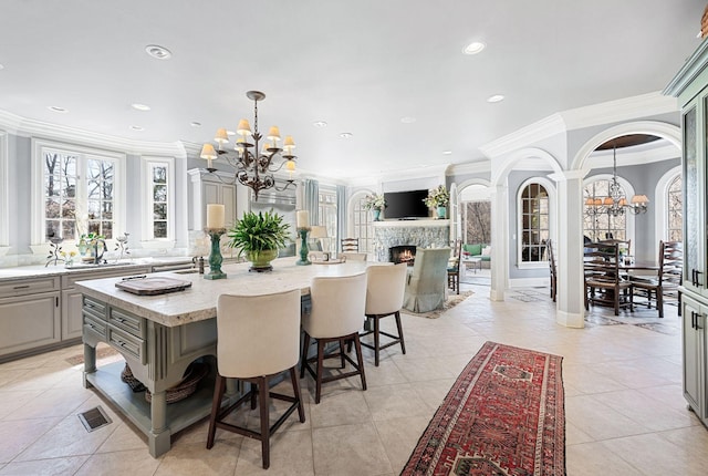 kitchen with a chandelier, gray cabinetry, ornamental molding, a kitchen island, and a warm lit fireplace