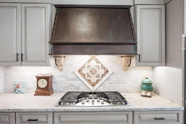 kitchen with custom exhaust hood, stainless steel gas cooktop, backsplash, and gray cabinets