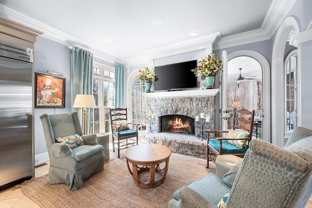 living room with a stone fireplace, crown molding, ceiling fan, baseboards, and tile patterned floors