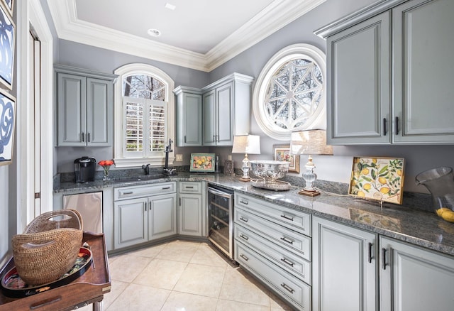 kitchen with wine cooler, gray cabinetry, light tile patterned floors, dark stone counters, and ornamental molding