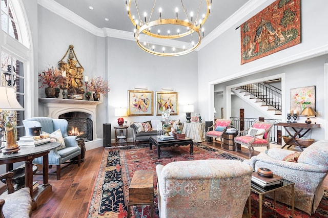 living area featuring a towering ceiling, ornamental molding, a chandelier, hardwood / wood-style flooring, and a warm lit fireplace