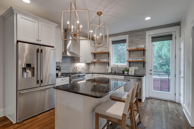 kitchen with high end appliances, open shelves, a sink, wall chimney range hood, and a chandelier