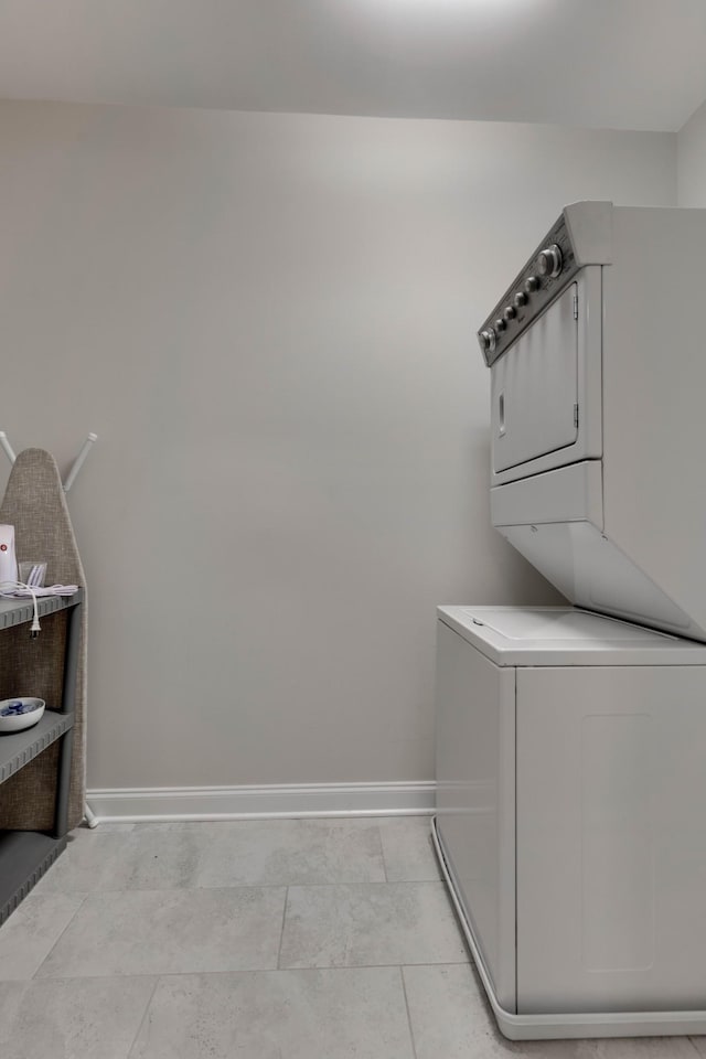 laundry room featuring stacked washer / drying machine, baseboards, and light tile patterned flooring