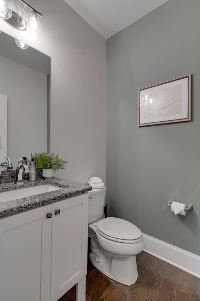 half bath featuring toilet, wood finished floors, vanity, and baseboards