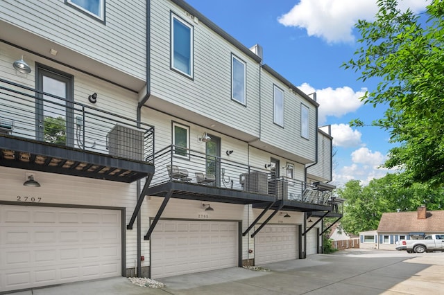 rear view of house with an attached garage, concrete driveway, and a balcony