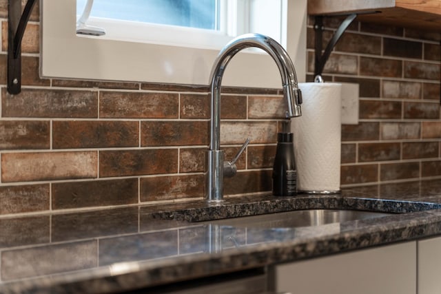 kitchen view of dark stone counters, white cabinetry, and a sink