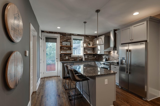 kitchen featuring premium appliances, open shelves, wall chimney range hood, dark wood-type flooring, and decorative backsplash
