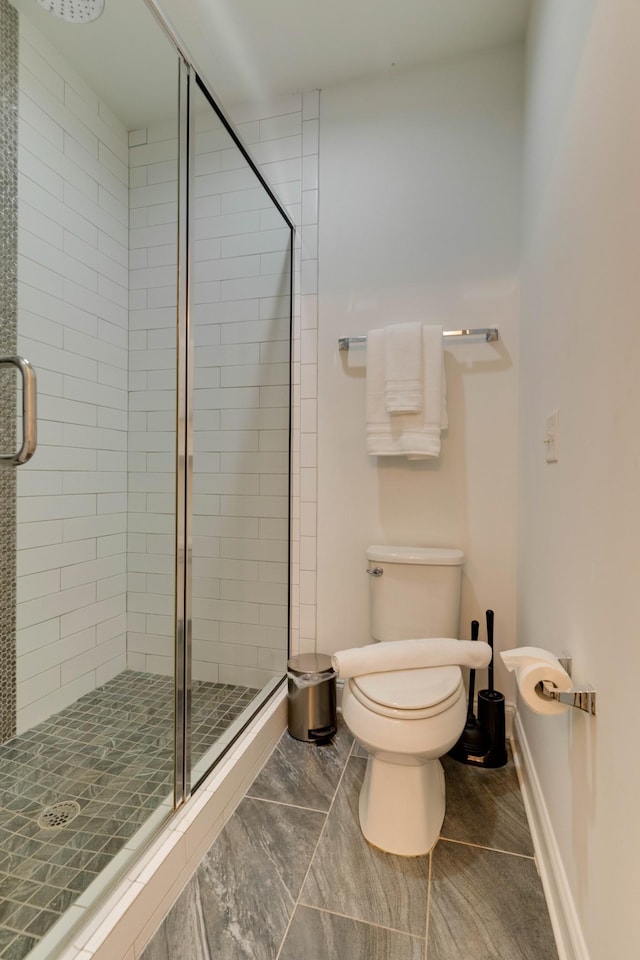 bathroom featuring a stall shower, toilet, marble look tiles, and baseboards