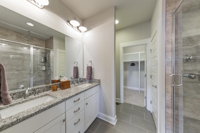 full bathroom with a shower stall, tile patterned floors, a walk in closet, double vanity, and baseboards