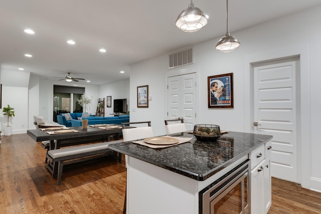 kitchen featuring stainless steel microwave, white cabinets, ceiling fan, wood finished floors, and decorative light fixtures