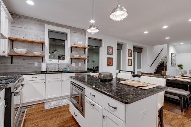 kitchen featuring stainless steel appliances, open shelves, a sink, light wood-style flooring, and decorative backsplash