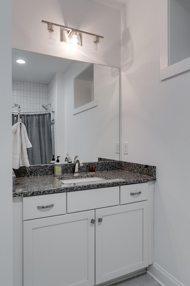 full bath with a tile shower, vanity, and baseboards