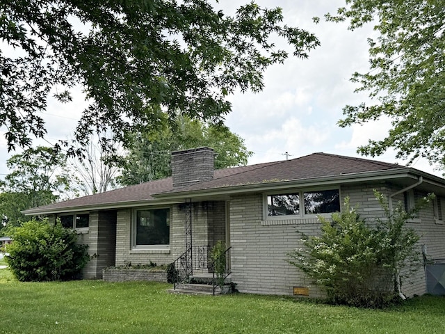 back of property featuring brick siding, a chimney, a yard, and crawl space