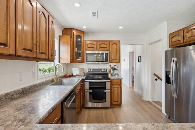 4588 Roy Thompson Rd, Mount Pleasant, TN 38474 - kitchen featuring appliances with stainless steel finishes, a sink, brown cabinetry, light wood-type flooring, and glass insert cabinets