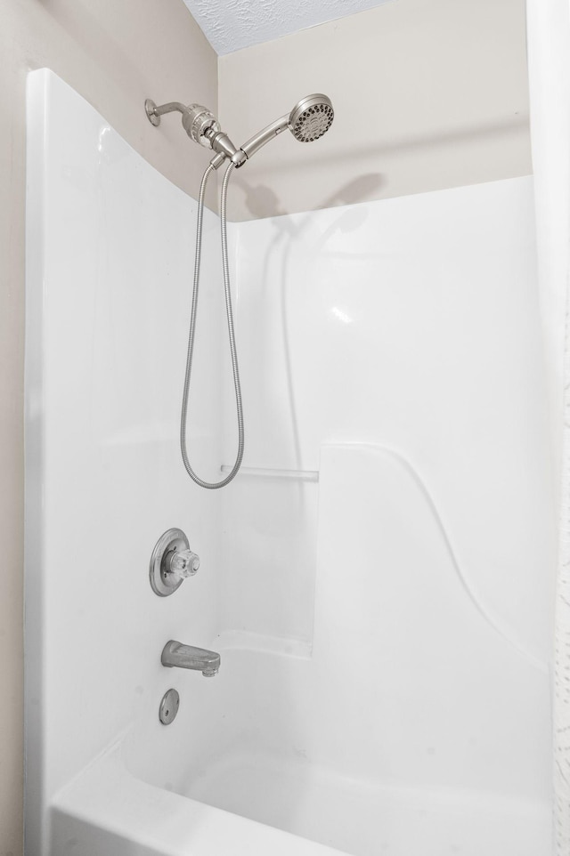 bathroom with a textured ceiling and shower / bathtub combination