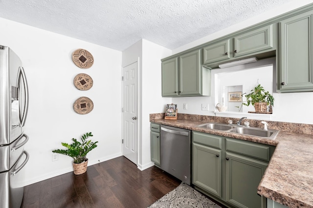 kitchen featuring stainless steel appliances, a sink, green cabinets, dark wood-style floors, and baseboards