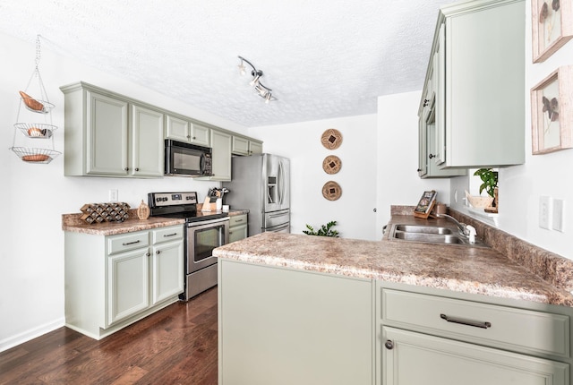 kitchen with stainless steel appliances, a sink, a textured ceiling, a peninsula, and dark wood-style floors