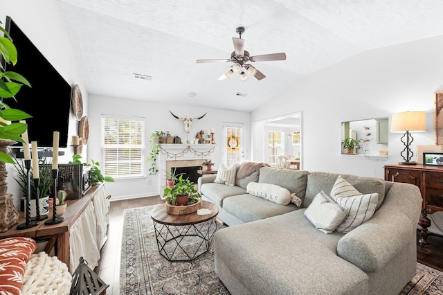 living room with vaulted ceiling, a ceiling fan, a fireplace, a textured ceiling, and wood finished floors
