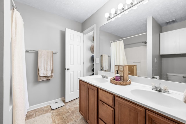 bathroom featuring baseboards, toilet, a textured ceiling, double vanity, and curtained shower