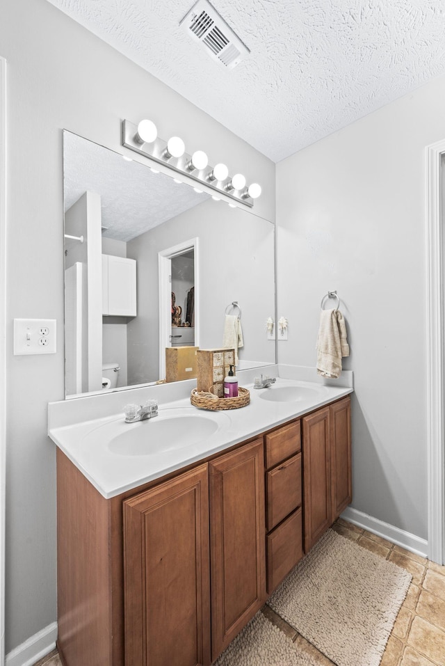 full bathroom with double vanity, toilet, a textured ceiling, and baseboards