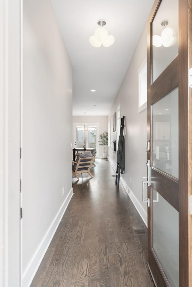 hall with dark wood finished floors, baseboards, and a chandelier
