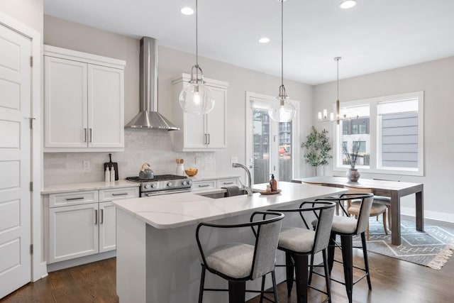 kitchen featuring a sink, wall chimney range hood, stainless steel gas range, decorative backsplash, and dark wood-style flooring