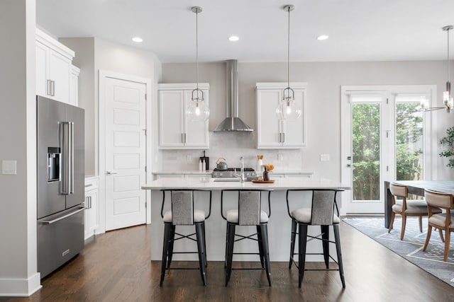 kitchen with high quality fridge, wall chimney exhaust hood, light countertops, dark wood-style floors, and tasteful backsplash