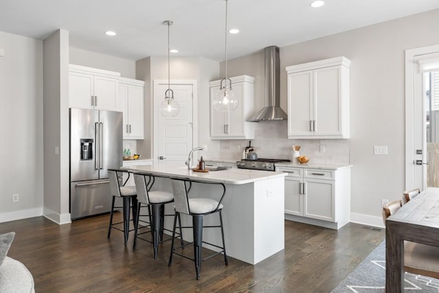 kitchen featuring stainless steel appliances, wall chimney exhaust hood, dark wood-type flooring, a kitchen breakfast bar, and decorative backsplash