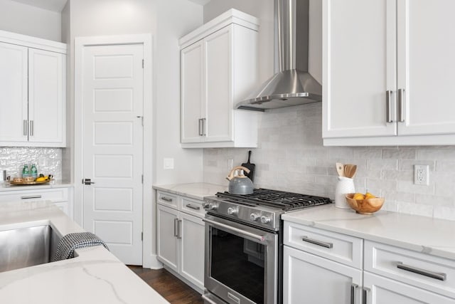 kitchen with stainless steel gas range oven, wall chimney range hood, backsplash, white cabinetry, and light stone counters