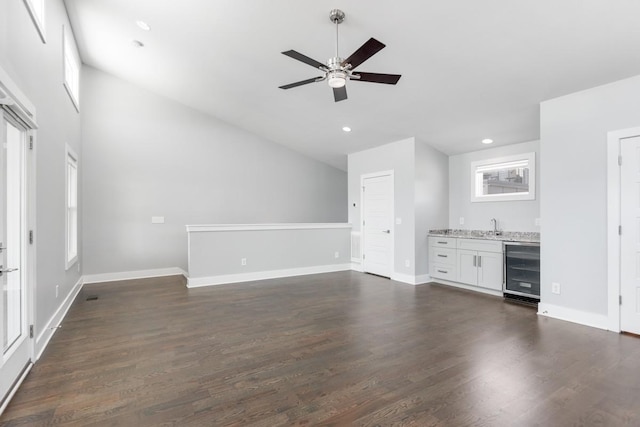 unfurnished living room featuring beverage cooler, lofted ceiling, a ceiling fan, baseboards, and wet bar