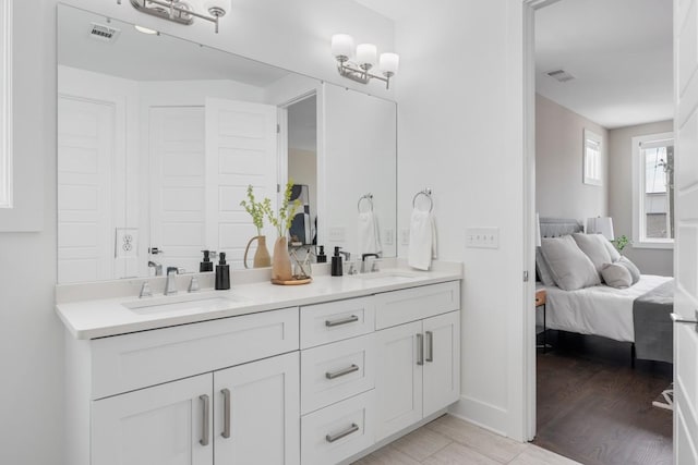 ensuite bathroom featuring double vanity, baseboards, and wood finished floors