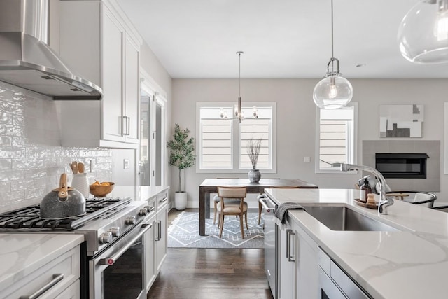 kitchen with appliances with stainless steel finishes, wall chimney range hood, dark wood-type flooring, a sink, and white cabinets