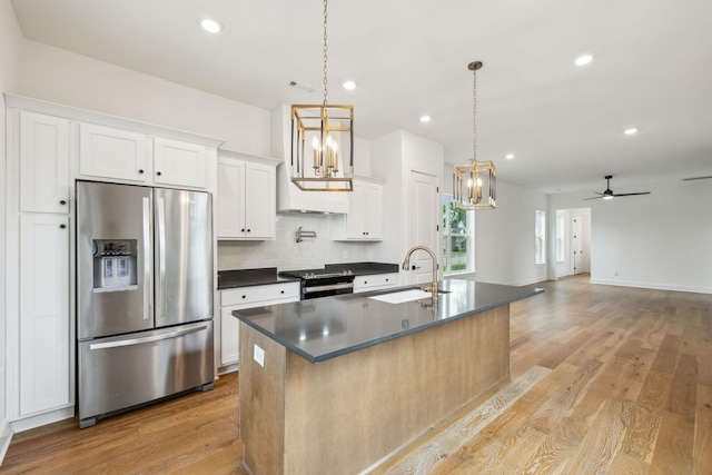 kitchen with appliances with stainless steel finishes, dark countertops, a sink, light wood finished floors, and white cabinetry