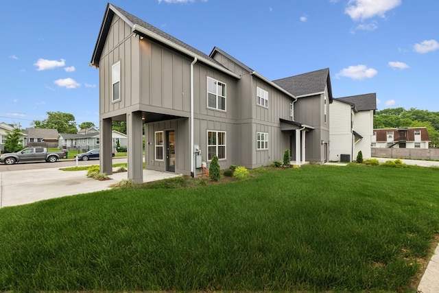 rear view of house featuring board and batten siding, a lawn, driveway, and a shingled roof
