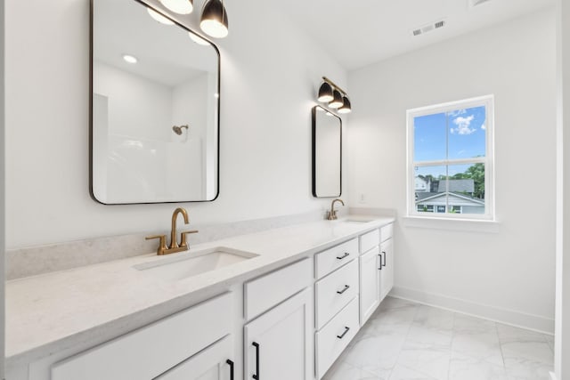 full bathroom with marble finish flooring, double vanity, baseboards, and a shower