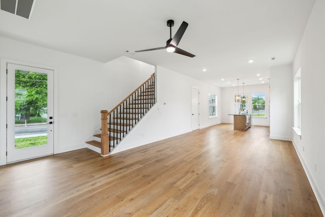 unfurnished living room with stairs, light wood-type flooring, recessed lighting, ceiling fan, and baseboards