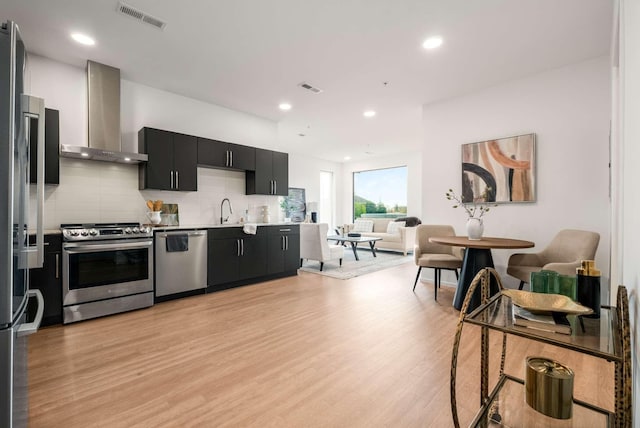 kitchen featuring appliances with stainless steel finishes, wall chimney exhaust hood, dark cabinets, open floor plan, and tasteful backsplash