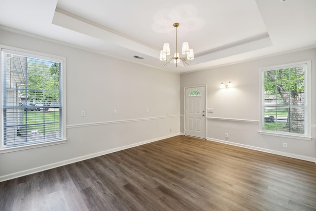 empty room featuring a raised ceiling, ornamental molding, a chandelier, and wood finished floors