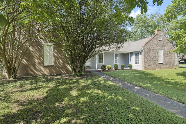 view of front of house with a chimney, a front lawn, brick siding, and roof with shingles