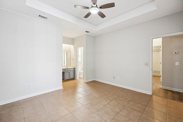 empty room featuring a ceiling fan, a tray ceiling, light tile patterned flooring, and baseboards