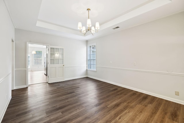 empty room featuring a chandelier, dark wood-type flooring, a tray ceiling, healthy amount of natural light, and crown molding